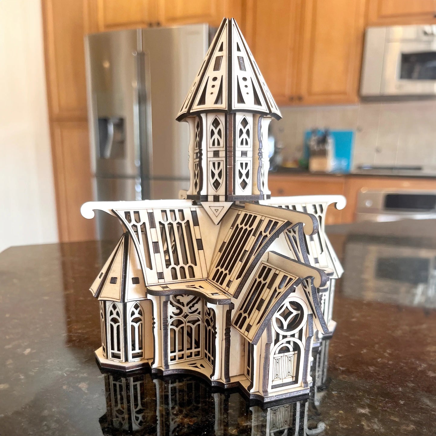 Assembled laser cut plywood gothic palace model with dark burnt edges placed on a reflective kitchen counter top.