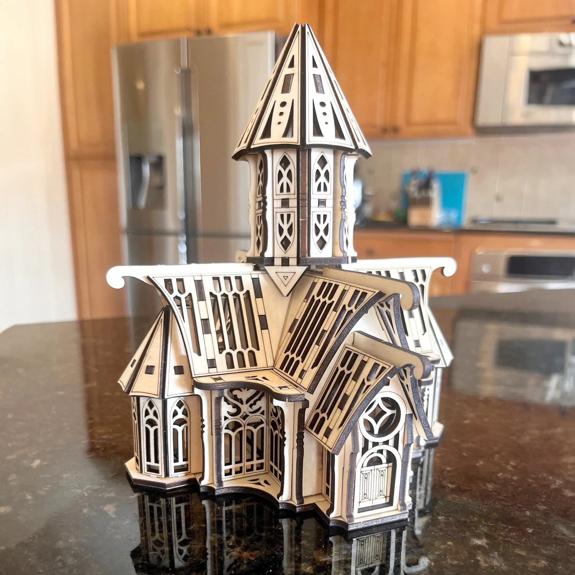 Assembled laser cut plywood gothic palace model with dark burnt edges placed on a reflective kitchen counter top.