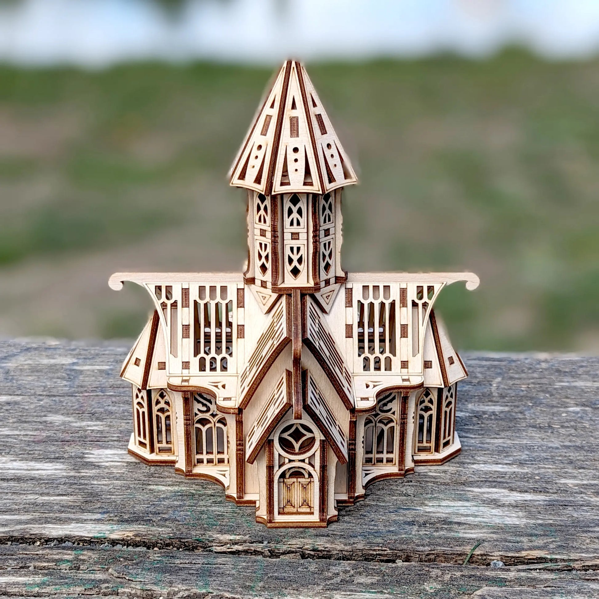 Front view of a miniature laser cut plywood gothic church with fine cutouts, staged outdoors on a weathered timber.