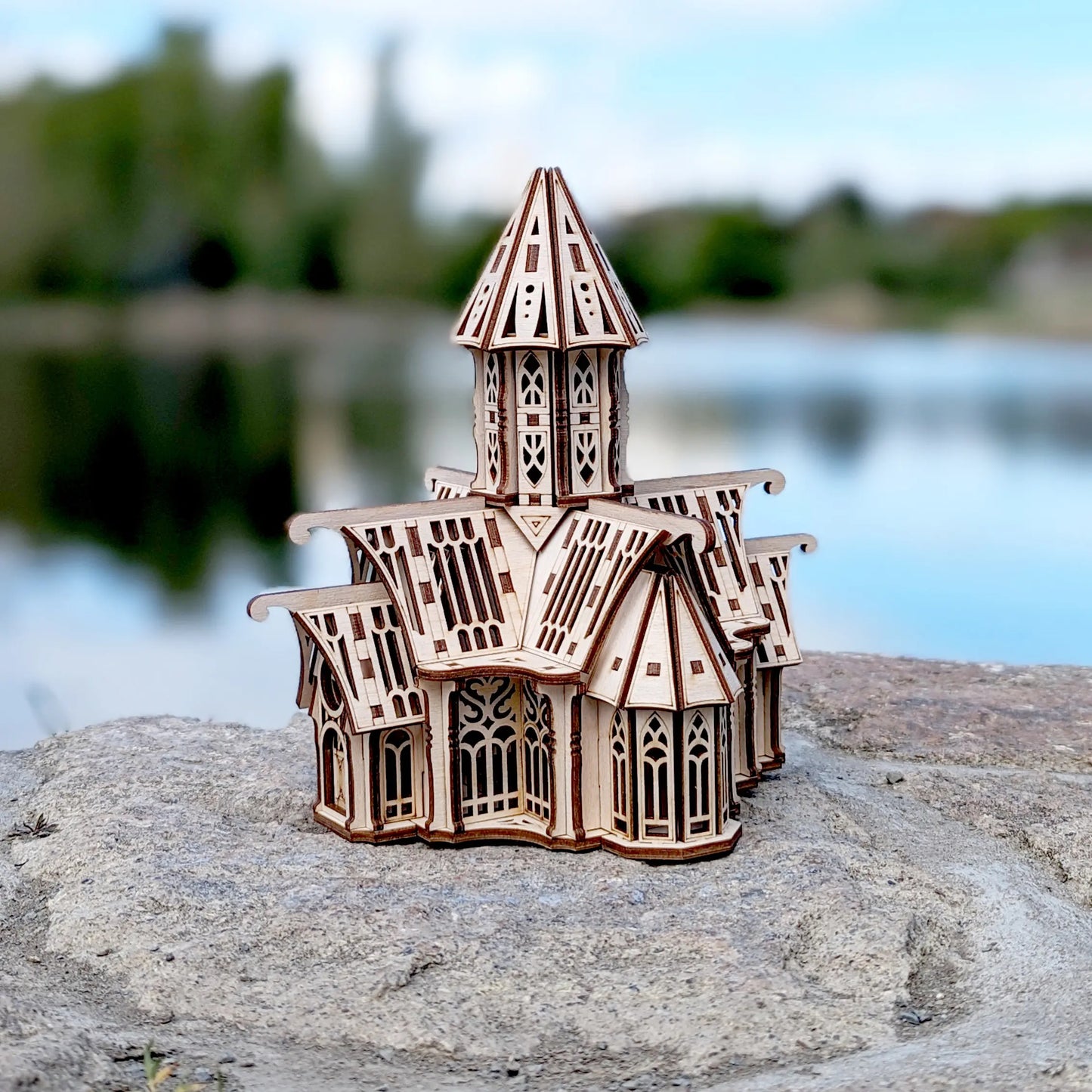 Three-quarter view of a laser cut plywood vintage mansion puzzle displayed on a natural rock by calm blue water.