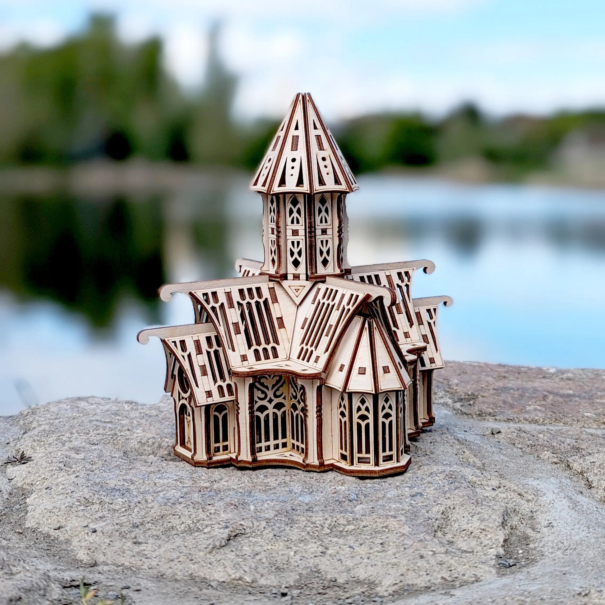 Three-quarter view of a laser cut plywood vintage mansion puzzle displayed on a natural rock by calm blue water.