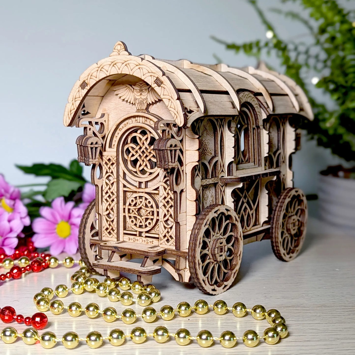 Wooden laser cit nomad wagon model of a decorative carriage with intricate designs, surrounded by flowers and beads on a light surface.