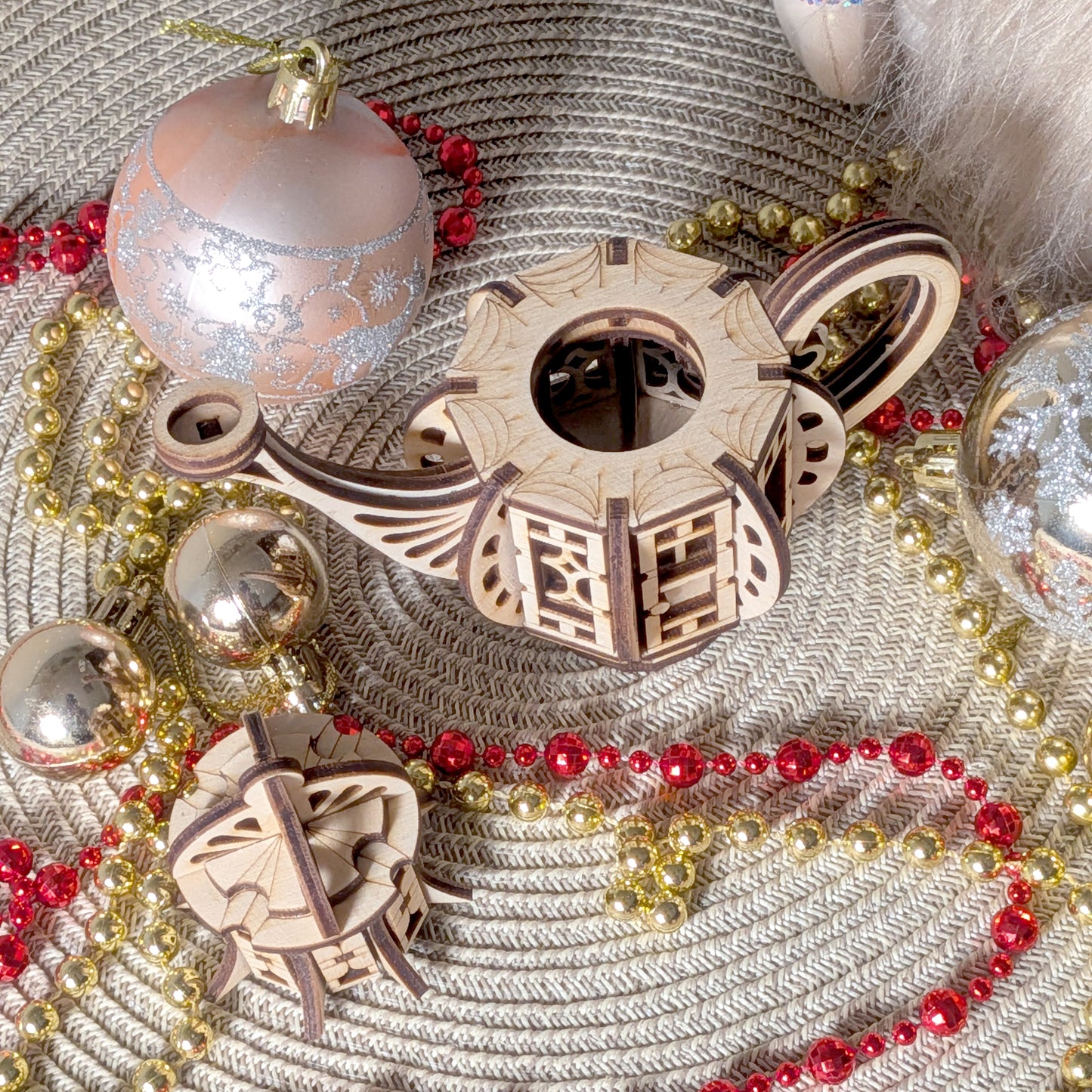 Top view of a laser cut wooden teapot fairy house with the lid removed, surrounded by gold and red beaded garlands and holiday ornaments.