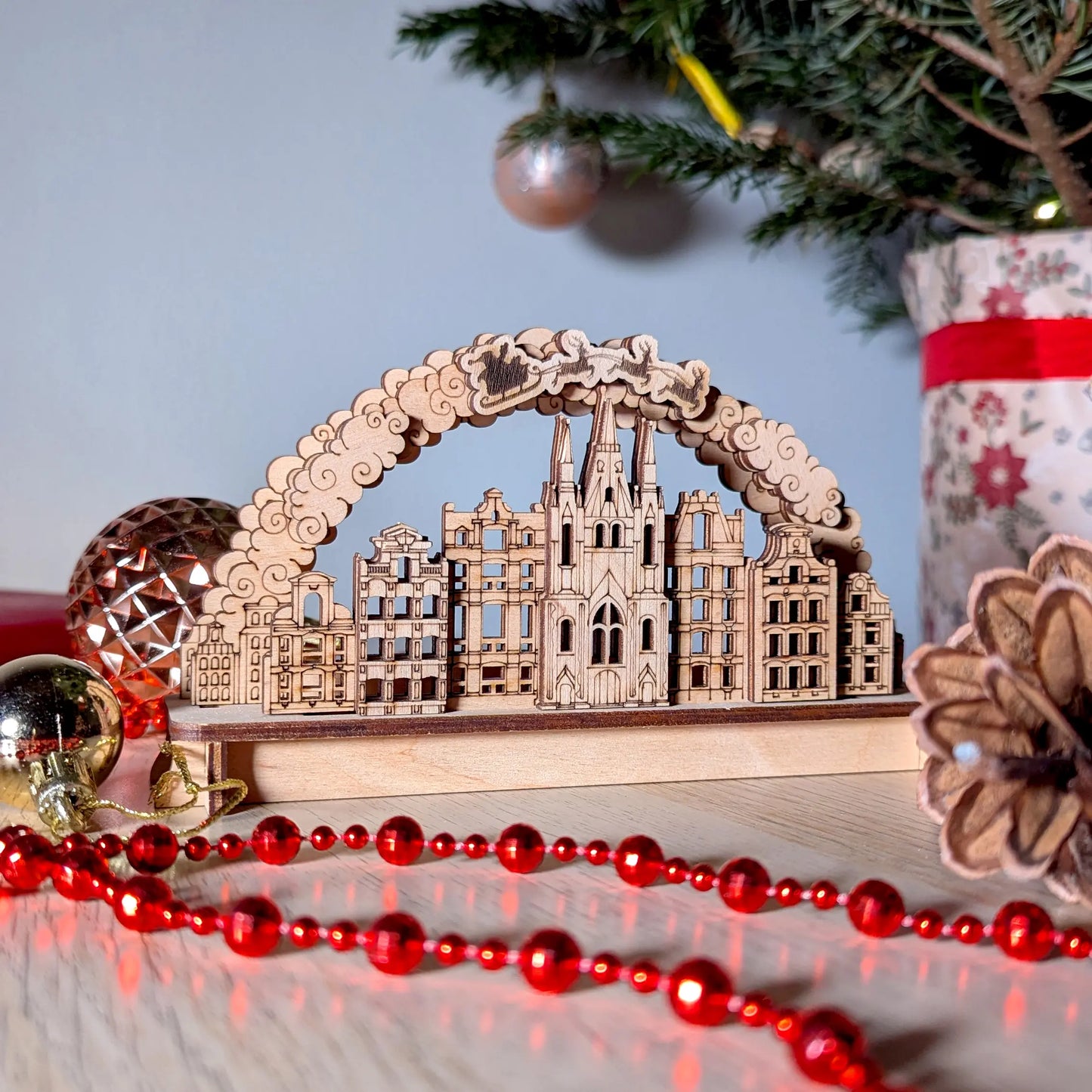 Beautifully staged front view of a miniature holiday Christmas town arch with festive ornaments, made of laser cut plywood.