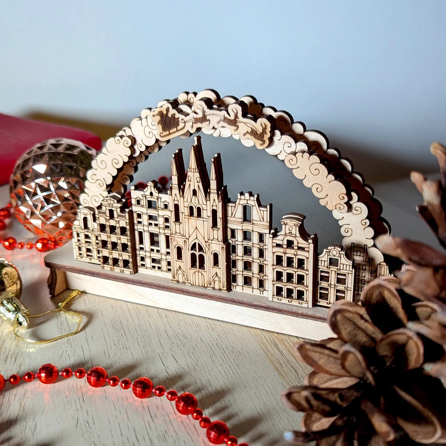 A left side angled perspective view of an intricate 3D holiday village arch puzzle crafted from layered laser cut plywood.
