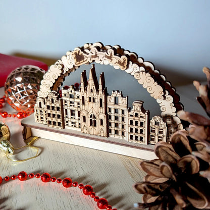 A left side angled perspective view of an intricate 3D holiday village arch puzzle crafted from layered laser cut plywood.