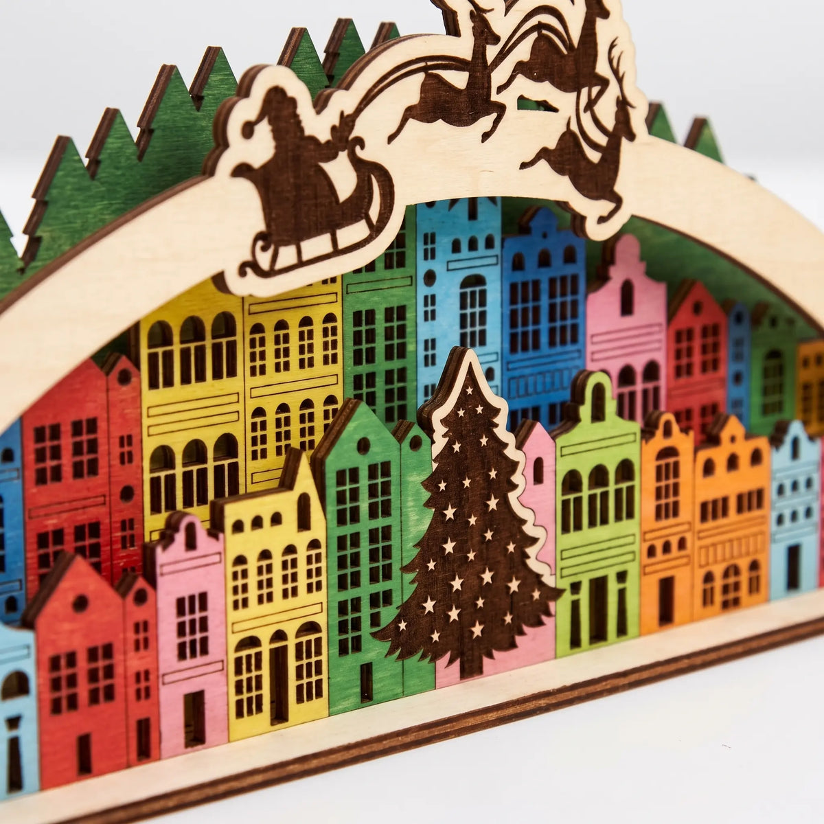 Close-up of colorful painted laser cut plywood Christmas arch showing town houses, wooden pine tree, and Santa sleigh.