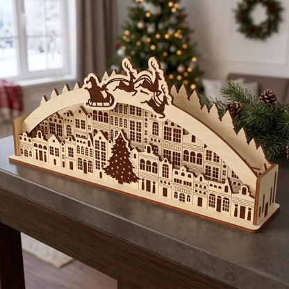 Unfinished laser cut plywood Christmas town arch diorama on table with spruce branch and illuminated holiday tree lights
