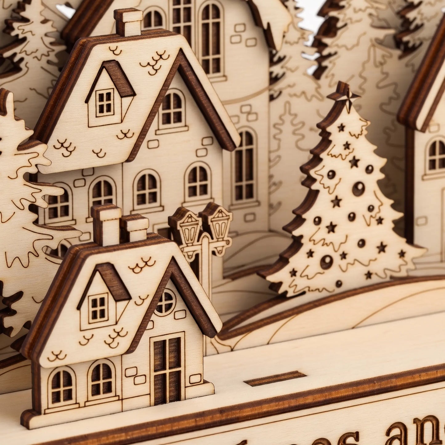 Close-up of a wooden miniature village scene with layered houses, trees, and a decorated Christmas tree, shown in warm natural wood tones.