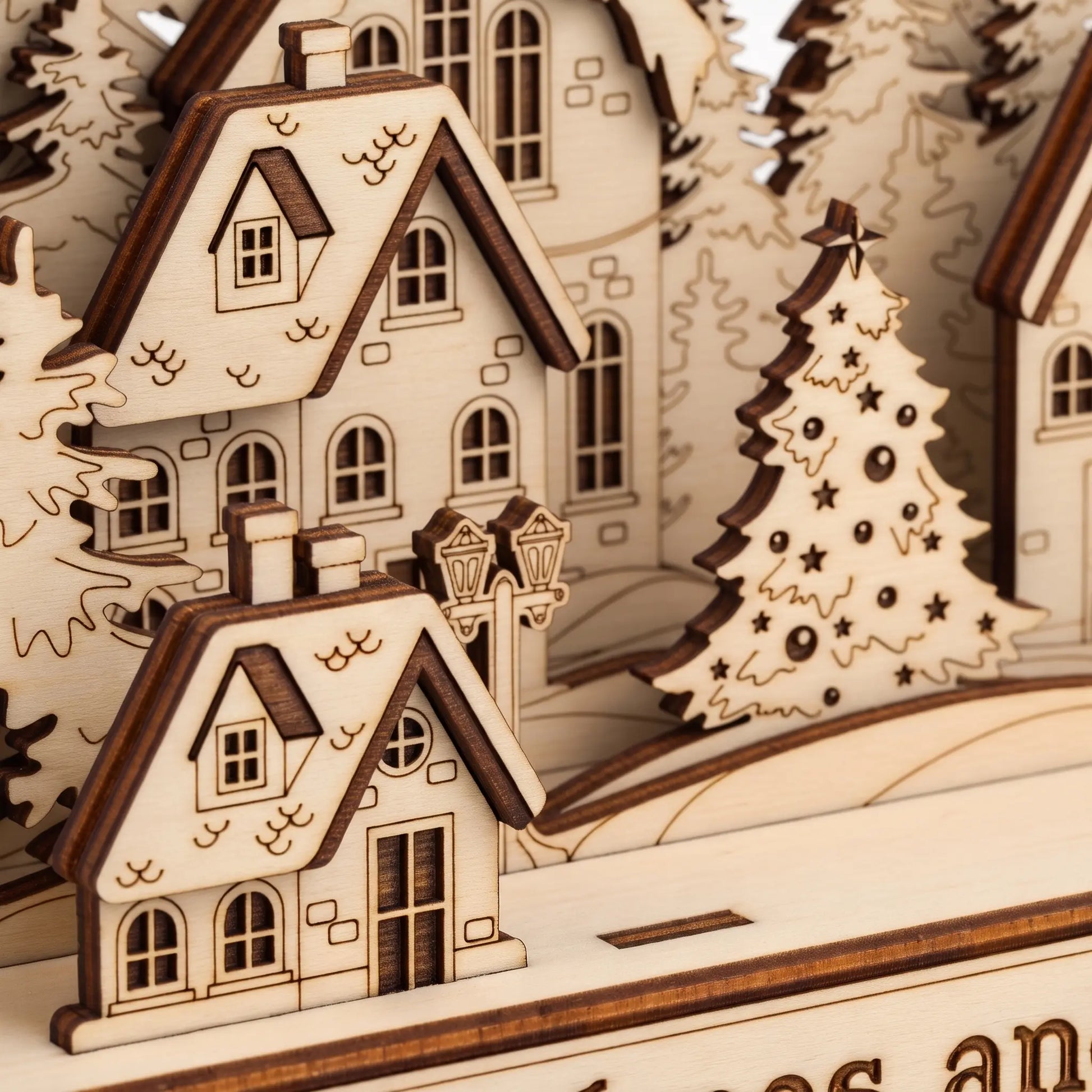 Close-up of a wooden miniature village scene with layered houses, trees, and a decorated Christmas tree, shown in warm natural wood tones.