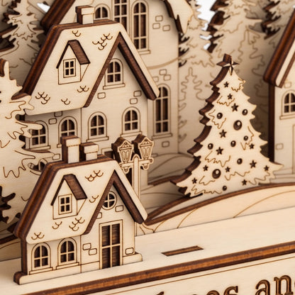 Close-up of a wooden miniature village scene with layered houses, trees, and a decorated Christmas tree, shown in warm natural wood tones.