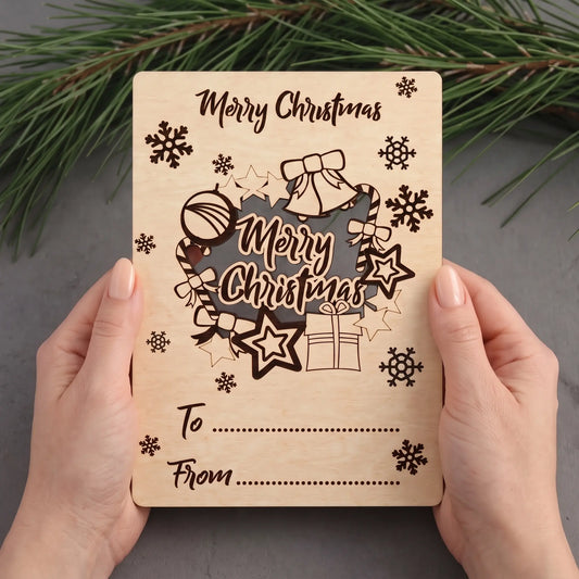 Hands hold laser cut plywood holiday greeting postcard with pop-out wreath cutout over gray table and pine.
