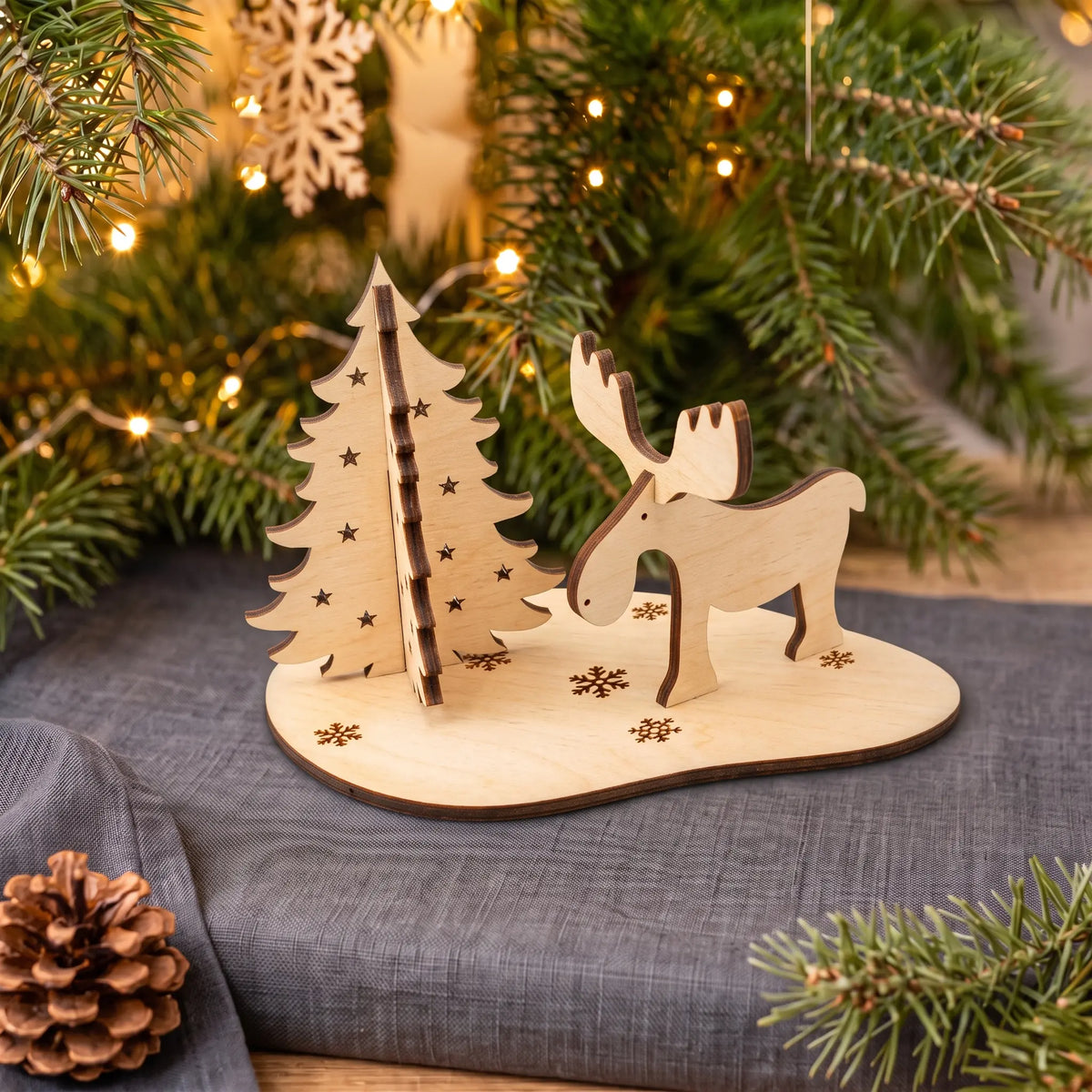 Assembled laser cut plywood moose and evergreen tree standing on snowflake stand by Christmas garland.