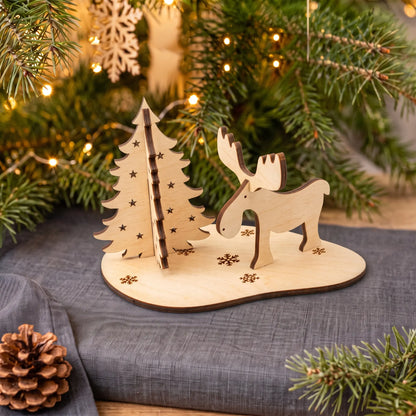 Assembled laser cut plywood moose and evergreen tree standing on snowflake stand by Christmas garland.