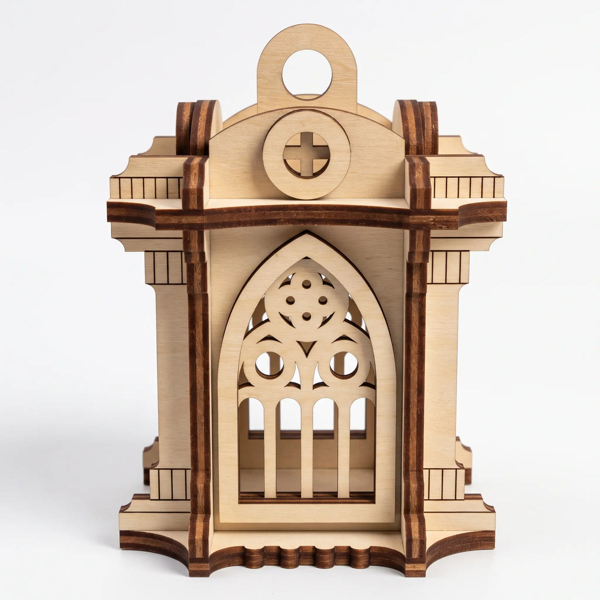 Front view of 3D laser cut plywood gothic chapel lantern with pointed arch and cross cutout over plain white backdrop.