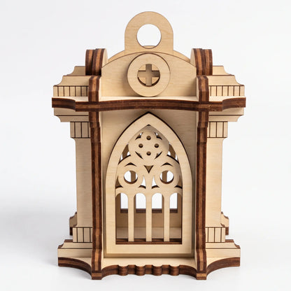 Front view of 3D laser cut plywood gothic chapel lantern with pointed arch and cross cutout over plain white backdrop.