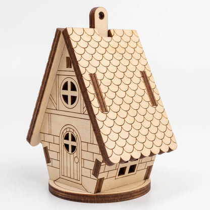 Front three-quarter view of laser cut plywood fairy cottage ornament with scalloped roof shingles on white background.