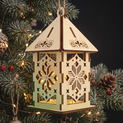 Illuminated laser cut plywood snowflake lantern ornament hanging on Christmas tree branch with pinecone