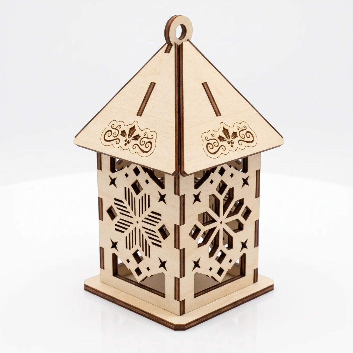 Unlit laser cut plywood lantern with carved snowflake patterns and floral roof details on white surface.