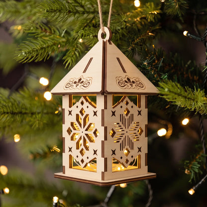 Glowing laser cut plywood Christmas lantern hung with twine against green fir branches and fairy lights.