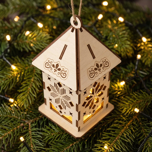 Top-down view of glowing laser cut plywood mini lantern sitting on fresh pine needles and fairy lights.