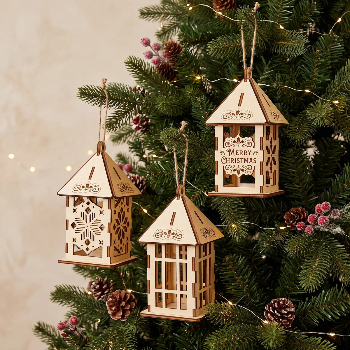 Three laser cut plywood Christmas lanterns hanging from twine on pine tree branches with red berries.