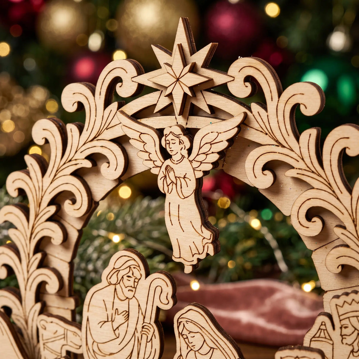 Close-up of laser cut plywood arch showing carved Bethlehem star and flying angel praying above holy family.