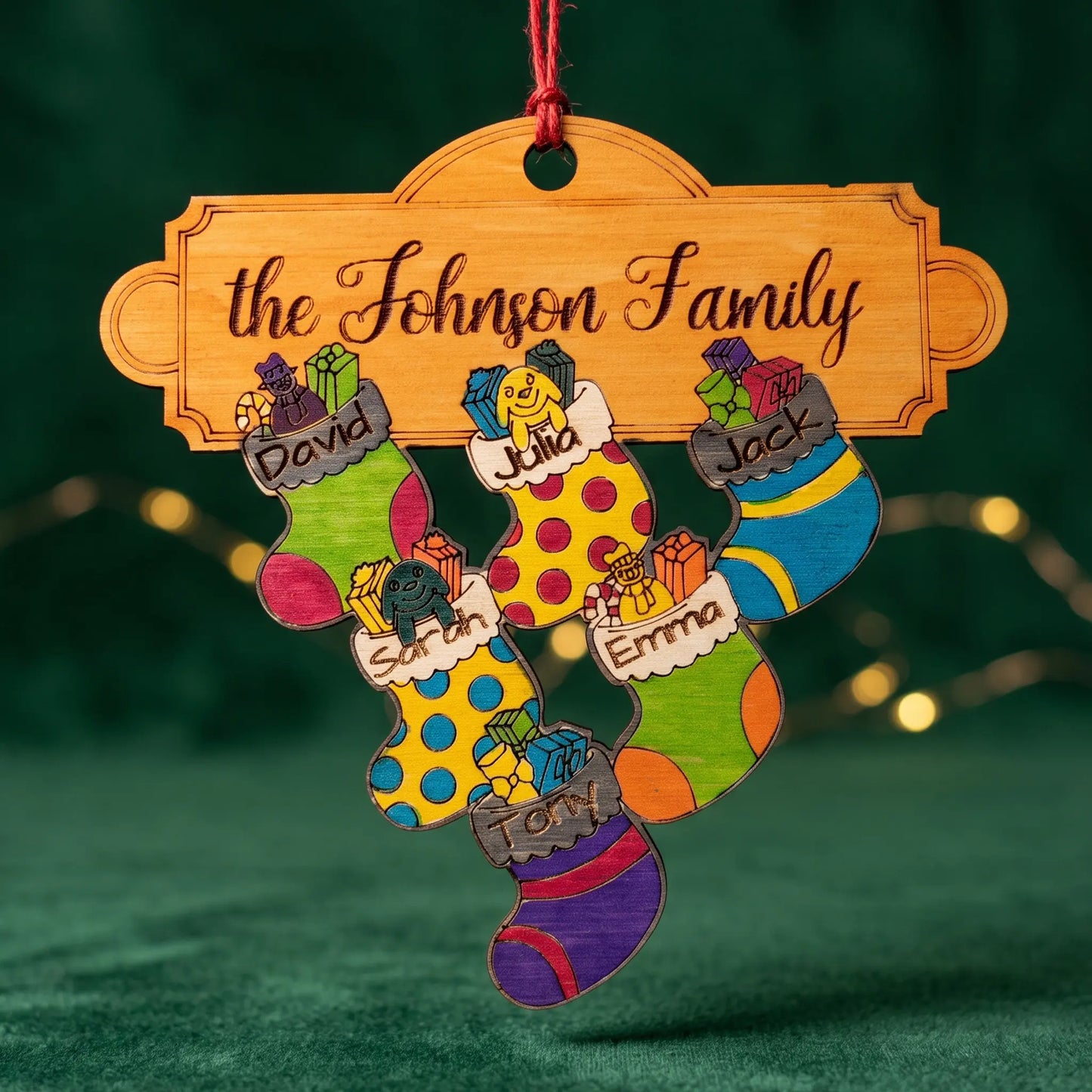 A personalized laser cut Christmas ornament shaped like a family name sign above four colorful hand-drawn stockings. 