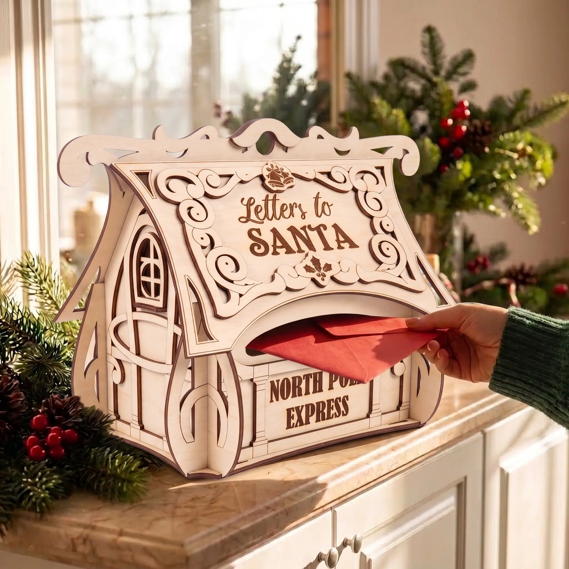 Hand slides red envelope into laser cut plywood Letters to Santa mailbox on kitchen counter by bright holiday window.