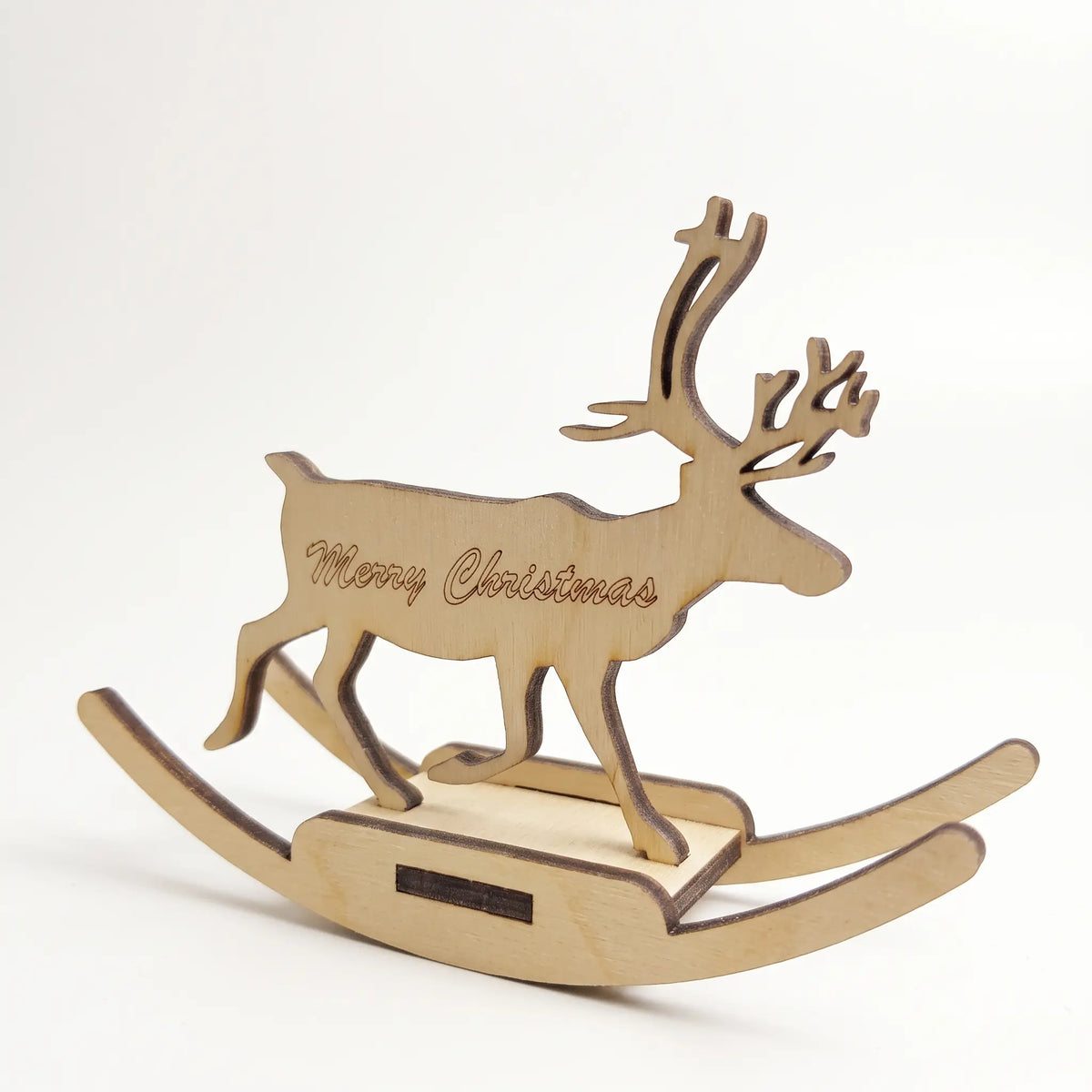 Side view of rocking reindeer made of laser cut plywood with Merry Christmas engraving on white backdrop.