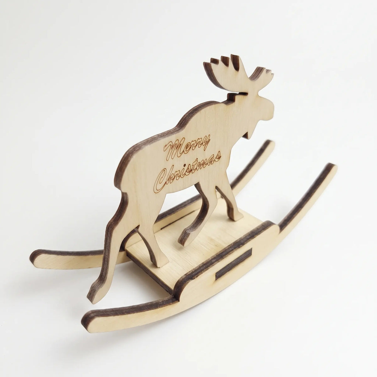 High-angle perspective of laser cut plywood rocking moose toy with carved holiday script on white base.