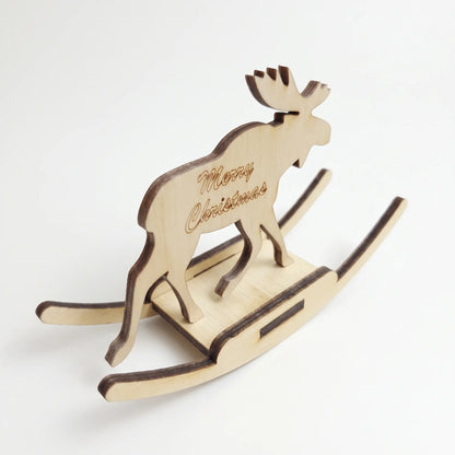 High-angle perspective of laser cut plywood rocking moose toy with carved holiday script on white base.