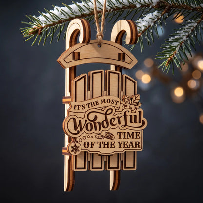 A wooden laser cut sledding ornament hanging from a pine branch, with the engraved text 'IT'S THE MOST Wonderful TIME OF THE YEAR' on a dark blurred background with warm bokeh lights.
