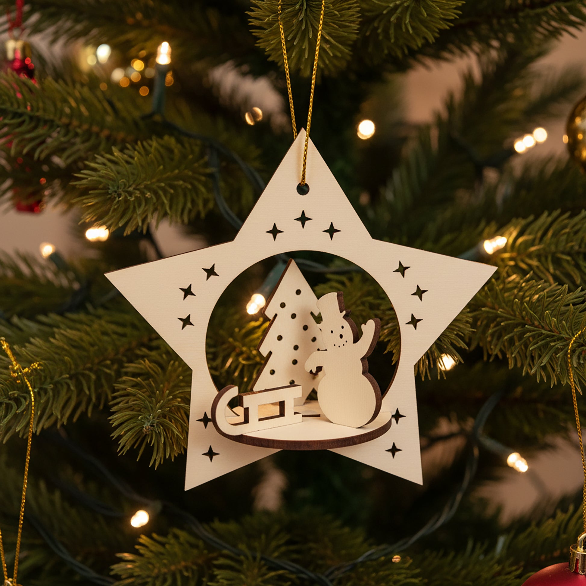 Intricate laser cut Christmas Snowman toy featuring a 3D snowy scene of a smiling snowman, holiday tree and present inside a star silhouette, set against a warm lighted Christmas tree background.