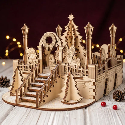 Staged photo of a laser cut plywood Christmas village on a white wood table with pinecones, faux snow, and fairy lights