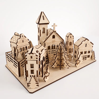 High-angle perspective view of laser cut plywood holiday village diorama with central church, trees, and figurines.