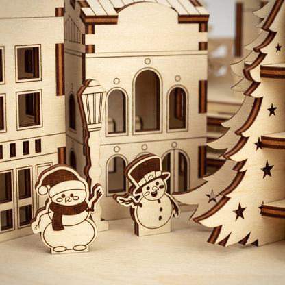 Close-up of laser cut plywood miniature snowmen standing by street lantern and detailed building facades on light wood