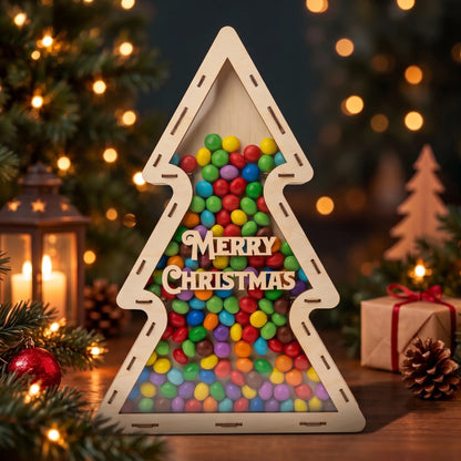 Front view of laser cut plywood tree candy dispenser with Merry Christmas text, surrounded by lights and cones.