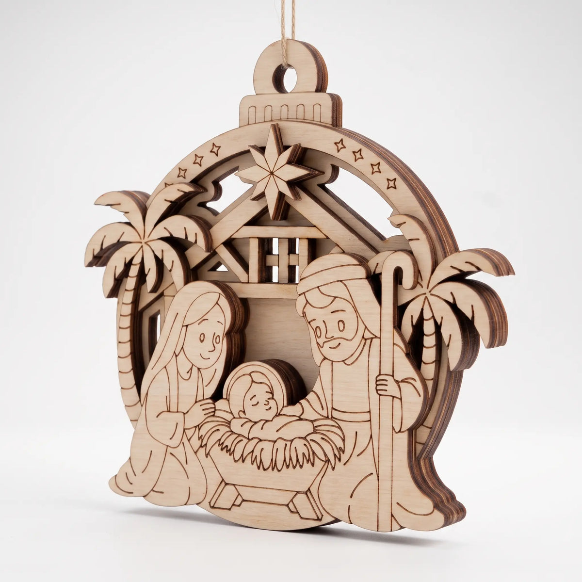 Angled view of layered laser cut plywood nativity bauble ornament with holy family figures, on white background.