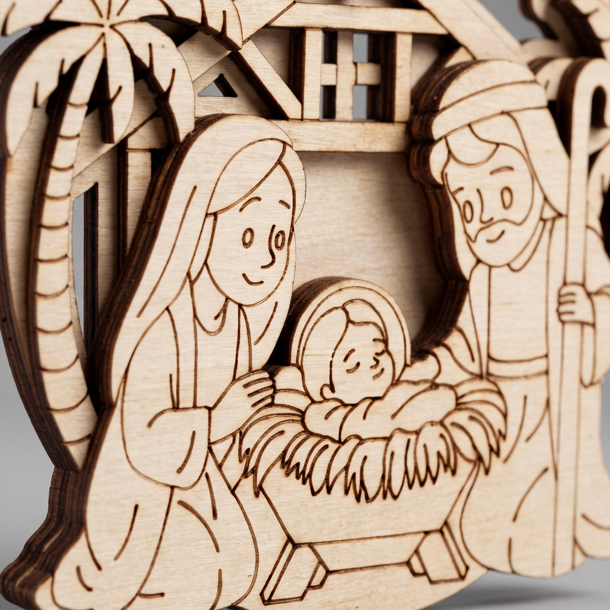 Extreme close-up of baby Jesus and holy family engraved details on laser cut plywood nativity bauble ornament.
