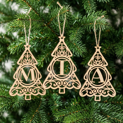 Three laser cut plywood monogram Christmas tree ornaments spelling MIA hanging by twine strings among evergreen branches.