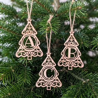 Staggered set of three laser cut plywood tree letter ornaments A, B, and C hanging by twine strings on festive pine tree.