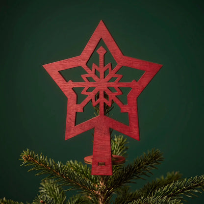 Red painted laser cut plywood snowflake star tree topper mounted on a green Christmas tree top against dark backdrop.