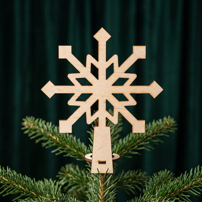 Laser cut plywood snowflake tree topper with ring base fixed on top of a Christmas pine branch against green backdrop.
