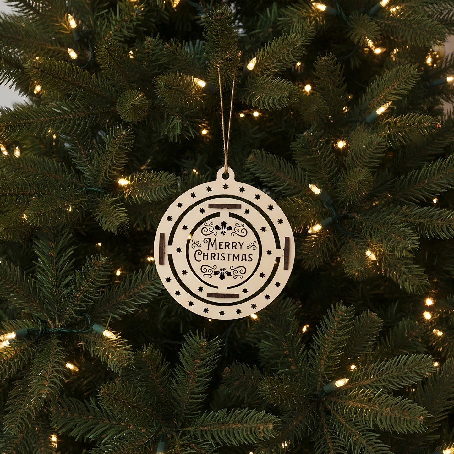 Interactive laser cut Christmas tree toy Xmas featuring a rotating holly wreath design on a round hanging ornament engraved with festive wishes, set against a softly lit Christmas tree background.