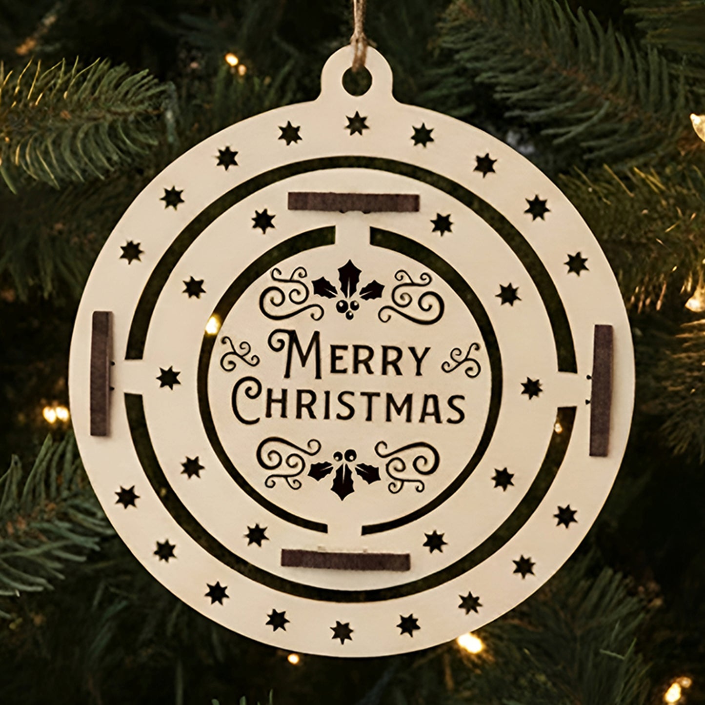 Laser cut wooden Christmas tree toy Xmas with a spinning inner ring of holly leaves and "Merry Christmas" greeting surrounded by star cut-outs, displayed against a warm twinkling Christmas tree background.