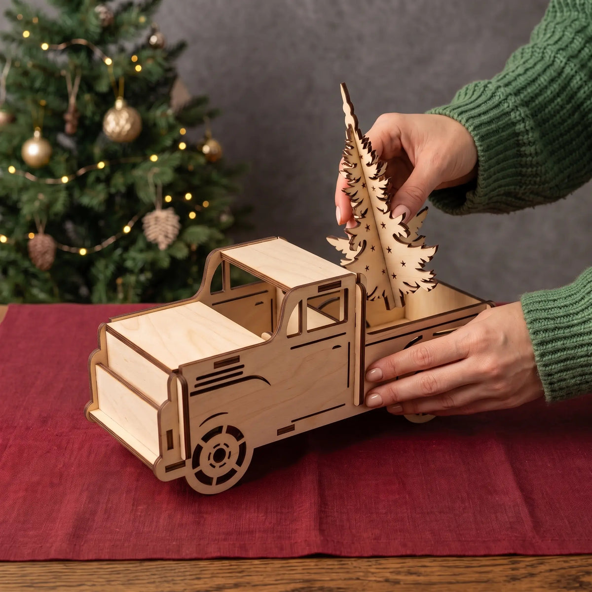 Hands place slotted laser cut plywood Christmas tree into cargo bed of assembled wooden pickup truck model.