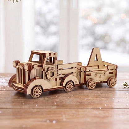 Laser cut plywood vintage Christmas truck with wreath and wagon hauling letter A on wooden table with snowy window view.