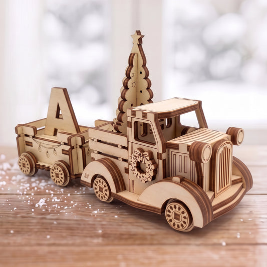 Laser cut plywood vintage Christmas truck with tree and wagon hauling letter A on snowy tabletop near window.