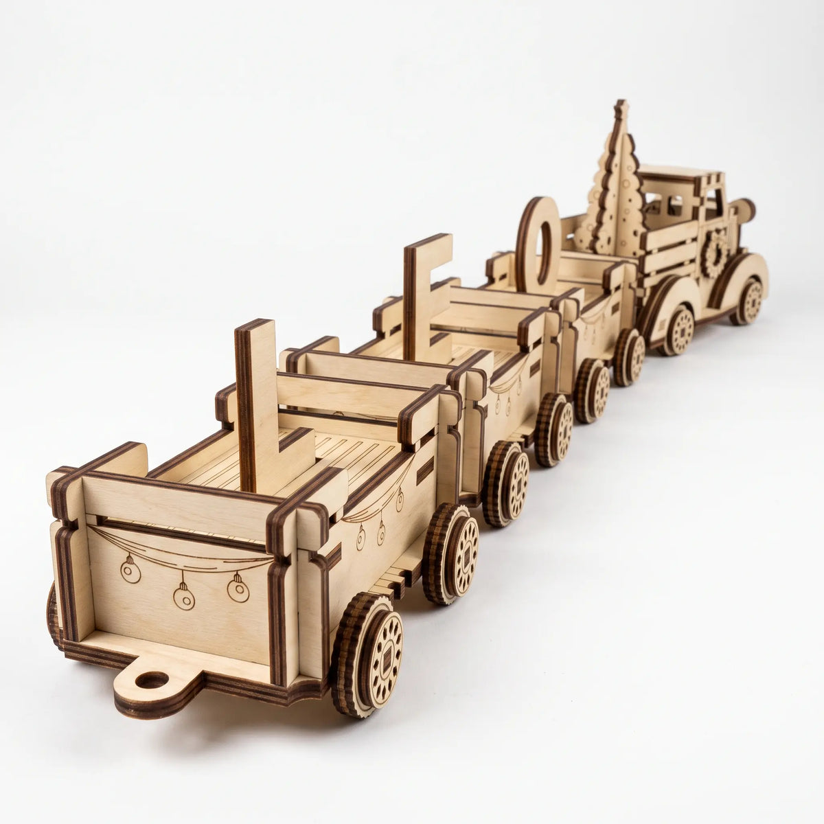 Rear perspective view of laser cut plywood holiday train cars carrying name letters pulled by vintage truck on white base.